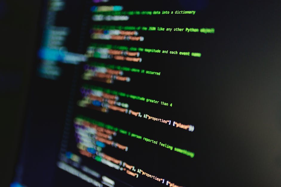 Close-up view of a computer screen displaying lines of colorful programming code on a dark background. The code includes syntax elements in green, orange, purple, and blue, with some lines slightly ou